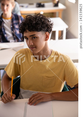 Teenage male student and female classmates writing in spiral notebook at class Teenage male student and female classmates writing in spiral notebook at class 141539625