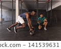 Male african american trainee, trainer guiding kettlebell climbers at gym with tablet, stopwatch 141539631