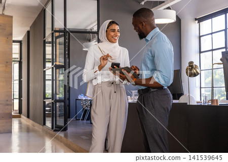 Diverse coworkers in business attire holding smartphone and tablet near desk in open-plan office Diverse coworkers in business attire holding smartphone and tablet near desk in open-plan office 141539645