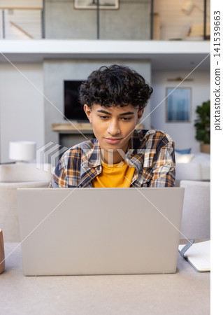 Asian man typing on silver laptop at living room table with ceramic mug, notebook Asian man typing on silver laptop at living room table with ceramic mug, notebook 141539663
