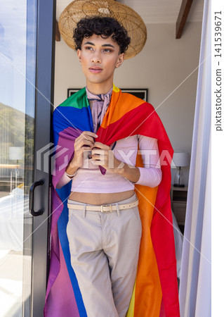 Asian man standing in sliding glass balcony doorway, wearing top, rainbow pride flag, scarf Asian man standing in sliding glass balcony doorway, wearing top, rainbow pride flag, scarf 141539671