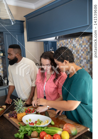 Diverse friends preparing fruit salad at kitchen with large cutting board and mixing bowl 141539686