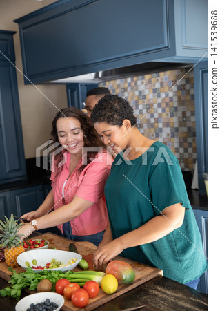Diverse friends slicing fruits for salad together in kitchen with wooden board, ceramic bowls 141539688