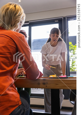 Diverse female coworkers collaborating over table in meeting room with colorful sticky notes Diverse female coworkers collaborating over table in meeting room with colorful sticky notes 141539745