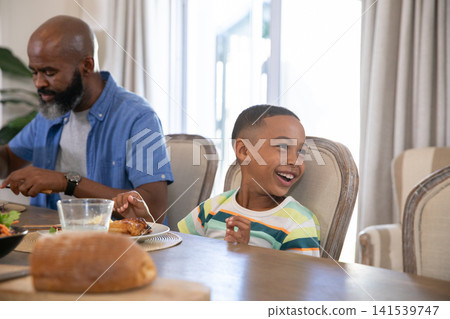 African American father and son sharing lunch in home dining room with roasted chicken, copy space African American father and son sharing lunch in home dining room with roasted chicken, copy space 141539747