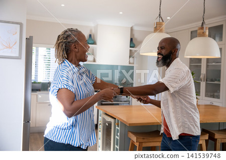 Senior African American couple dancing in home kitchen on island under pendant lights by fridge Senior African American couple dancing in home kitchen on island under pendant lights by fridge 141539748