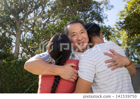 Asian family embracing each other in suburban backyard garden by fence and trimmed hedge Asian family embracing each other in suburban backyard garden by fence and trimmed hedge 141539750