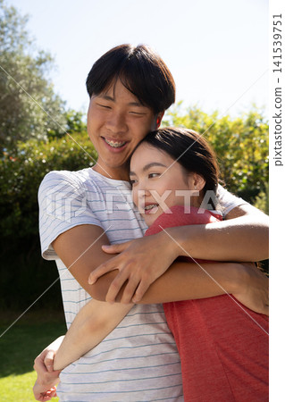 Asian couple hugging standing on lawn in backyard under sunlight showing braces and earrings Asian couple hugging standing on lawn in backyard under sunlight showing braces and earrings 141539751