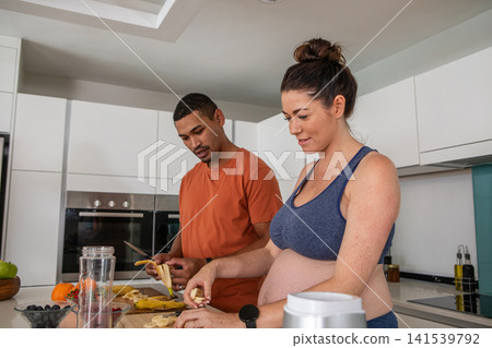 Diverse couple in sportswear chopping bananas and blending fruit at kitchen island for smoothie Diverse couple in sportswear chopping bananas and blending fruit at kitchen island for smoothie 141539792