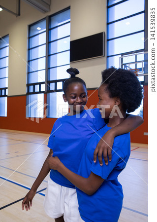 African american teenage girls smiling in shirts on basketball court with hoop and scoreboard 141539835