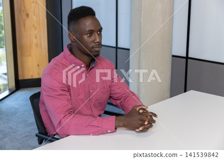 African american man sitting in black chair at modern office, clasping hands on white desk African american man sitting in black chair at modern office, clasping hands on white desk 141539842