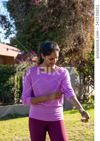 Indian woman rolling sleeves up, burgundy leggings in backyard with bougainvillea vines Indian woman rolling sleeves up, burgundy leggings in backyard with bougainvillea vines 141539851