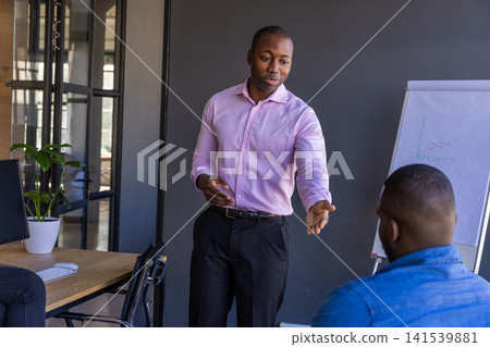 African american male colleagues analyzing line graph on flip chart in meeting room African american male colleagues analyzing line graph on flip chart in meeting room 141539881