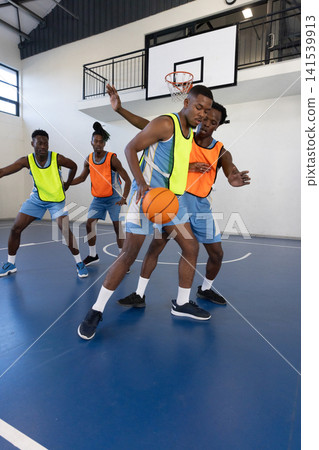 Four male basketball players wearing neon bibs dribbling orange basketball, defending on court Four male basketball players wearing neon bibs dribbling orange basketball, defending on court 141539913