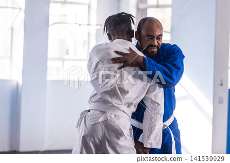 Adult african american men in blue gi gripping white gi, practicing grappling drill on mats Adult african american men in blue gi gripping white gi, practicing grappling drill on mats 141539929