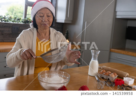 Senior Asian woman sifting flour through sieve at kitchen counter with cookie cutters, copy space Senior Asian woman sifting flour through sieve at kitchen counter with cookie cutters, copy space 141539958