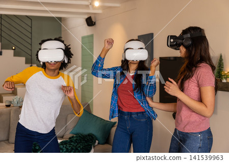 Diverse female friends standing in living room in white vr headsets exploring virtual world Diverse female friends standing in living room in white vr headsets exploring virtual world 141539963