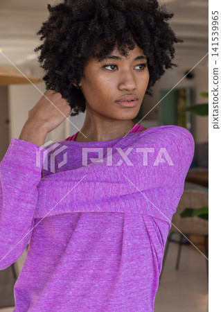 African american woman stretching arm across chest in lounge in purple top and pink sports bra African american woman stretching arm across chest in lounge in purple top and pink sports bra 141539965
