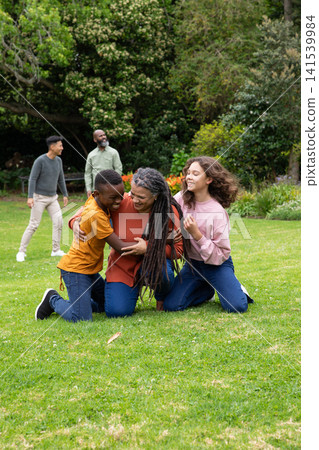 Diverse family kneeling hugging child boy and teenage hispanic girl on grass lawn Diverse family kneeling hugging child boy and teenage hispanic girl on grass lawn 141539984
