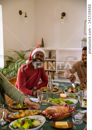 Diverse friends laughing, carving roast poultry around dining table at home with festive dishes Diverse friends laughing, carving roast poultry around dining table at home with festive dishes 141539988