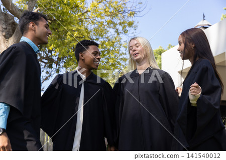 Diverse classmates in black graduation gowns smiling in courtyard celebrating graduation 141540012
