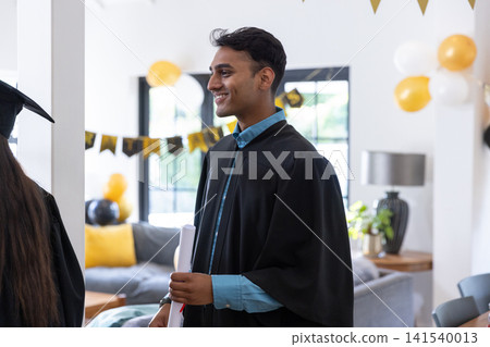 Asian friends celebrating graduation inside decorated living room with gowns balloons, diploma Asian friends celebrating graduation inside decorated living room with gowns balloons, diploma 141540013