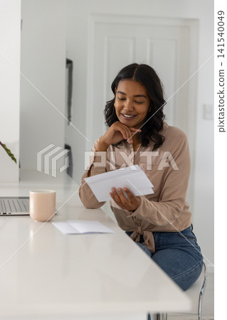 Woman reading letter while sitting at white kitchen countertop 141540049
