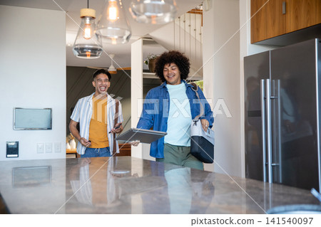 Diverse male friends walking into kitchen by stone island carrying smartphone and laptop Diverse male friends walking into kitchen by stone island carrying smartphone and laptop 141540097