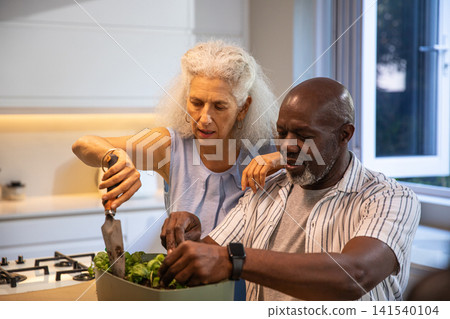 Senior couple chopping vegetables with chef's knife in large mixing bowl in home kitchen 141540104