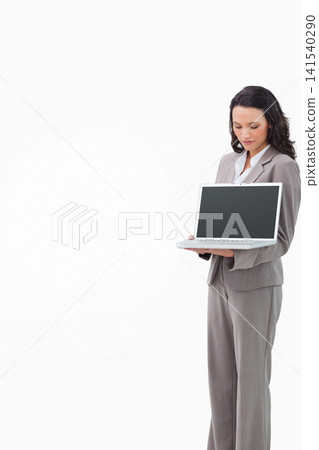 Businesswoman in grey suit holding white laptop with dark screen at studio right, copy space Businesswoman in grey suit holding white laptop with dark screen at studio right, copy space 141540290