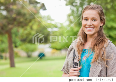 Female standing in park holding bag strap, wearing blue embroidered top, gray cardigan, copy space Female standing in park holding bag strap, wearing blue embroidered top, gray cardigan, copy space 141540291
