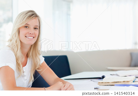 Woman wearing white top studying at table by sheer curtains with notebook, papers, copy space Woman wearing white top studying at table by sheer curtains with notebook, papers, copy space 141540314