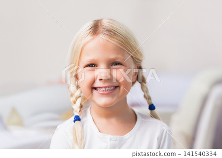 Child girl smiling broadly, facing camera in bedroom with blue elastics and white top Child girl smiling broadly, facing camera in bedroom with blue elastics and white top 141540334