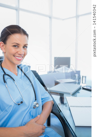 Female medical professional smiling while sitting at glass desk in clinical office with stethoscope Female medical professional smiling while sitting at glass desk in clinical office with stethoscope 141540342