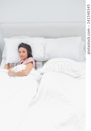 Woman lying left on bed in bedroom, holding pillow, white duvet, wearing pink top, copy space 141540345
