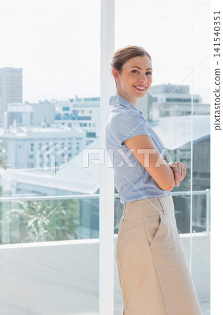 Mid-adult woman standing by glass window, balustrade in office, wearing blouse, skirt, copy space Mid-adult woman standing by glass window, balustrade in office, wearing blouse, skirt, copy space 141540351