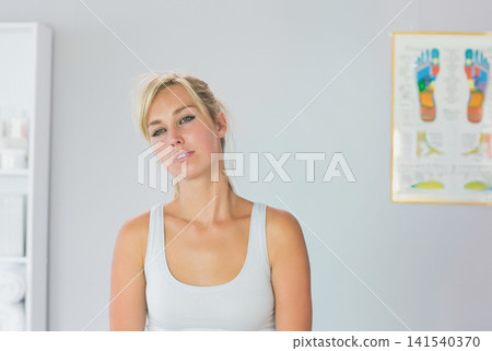 Female standing in clinic wearing white tank top, gazing at foot chart and rolled towels 141540370