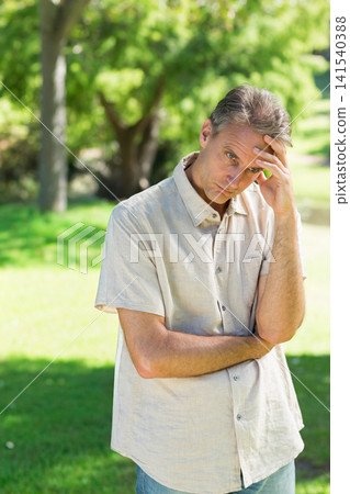 Middle-aged man standing on grassy park lawn wearing light beige button-up shirt and blue jeans Middle-aged man standing on grassy park lawn wearing light beige button-up shirt and blue jeans 141540388