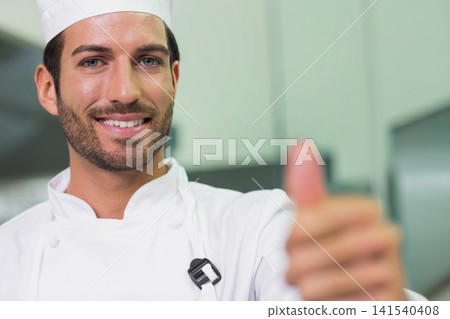 Male chef giving thumbs-up facing camera in professional kitchen in white jacket and hat with mic Male chef giving thumbs-up facing camera in professional kitchen in white jacket and hat with mic 141540408