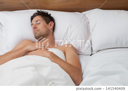 Man reclining on bed in bedroom, shirtless under white duvet with pillows, showing ring Man reclining on bed in bedroom, shirtless under white duvet with pillows, showing ring 141540409