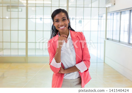 African American woman posing in office with frosted glass in coral blazer white shirt beige pants African American woman posing in office with frosted glass in coral blazer white shirt beige pants 141540424