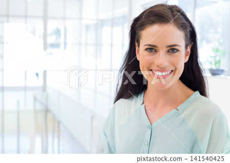 Adult woman smiling, standing right of office atrium glass, wearing light-blue blouse, copy space Adult woman smiling, standing right of office atrium glass, wearing light-blue blouse, copy space 141540425