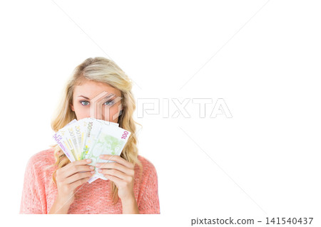 Adult female holding fanned Euro banknotes up to face at studio, wearing pink sweater, copy space Adult female holding fanned Euro banknotes up to face at studio, wearing pink sweater, copy space 141540437