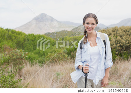 Adult female hiker standing right on grassy hillside holding trekking pole wearing pack, copy space Adult female hiker standing right on grassy hillside holding trekking pole wearing pack, copy space 141540438