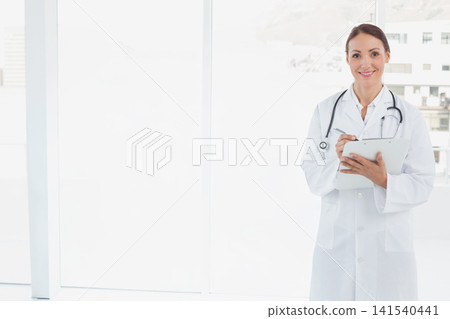 Woman doctor standing right in clinic writing on clipboard with stethoscope and labcoat, copy space Woman doctor standing right in clinic writing on clipboard with stethoscope and labcoat, copy space 141540441