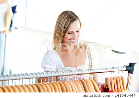 Adult female shopper standing at metal clothing rack with wooden hangers, reaching for red garment 141540444