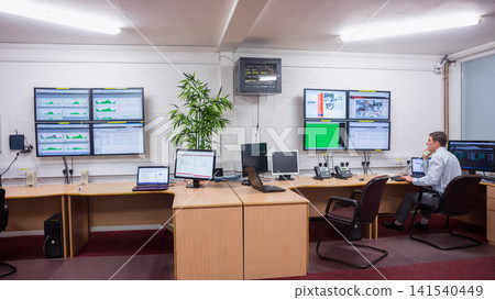 Male operator wearing shirt sitting at desk in control room monitoring screens cables, copy space Male operator wearing shirt sitting at desk in control room monitoring screens cables, copy space 141540449