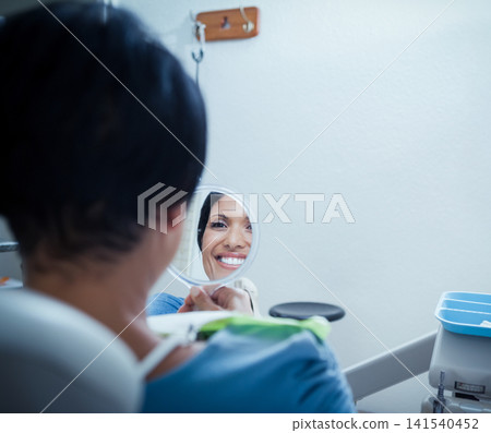 Mature woman holding round mirror while wearing dental bib, smiling at reflection in dental chair Mature woman holding round mirror while wearing dental bib, smiling at reflection in dental chair 141540452