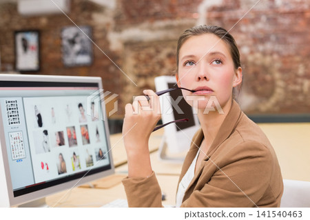 Female wearing brown blazer sitting at desk in studio holding glasses viewing monitor, copy space Female wearing brown blazer sitting at desk in studio holding glasses viewing monitor, copy space 141540463