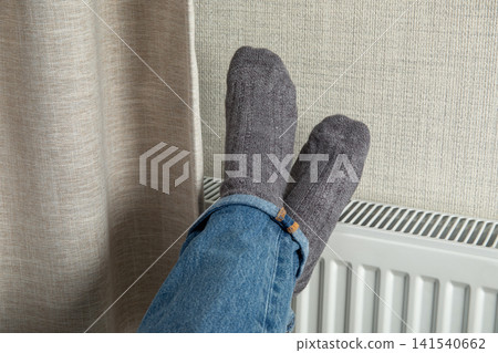 Heating season. Feet in cozy wool socks relax on radiator, enjoying warmth of heating season Heating season. Feet in cozy wool socks relax on radiator, enjoying warmth of heating season 141540662